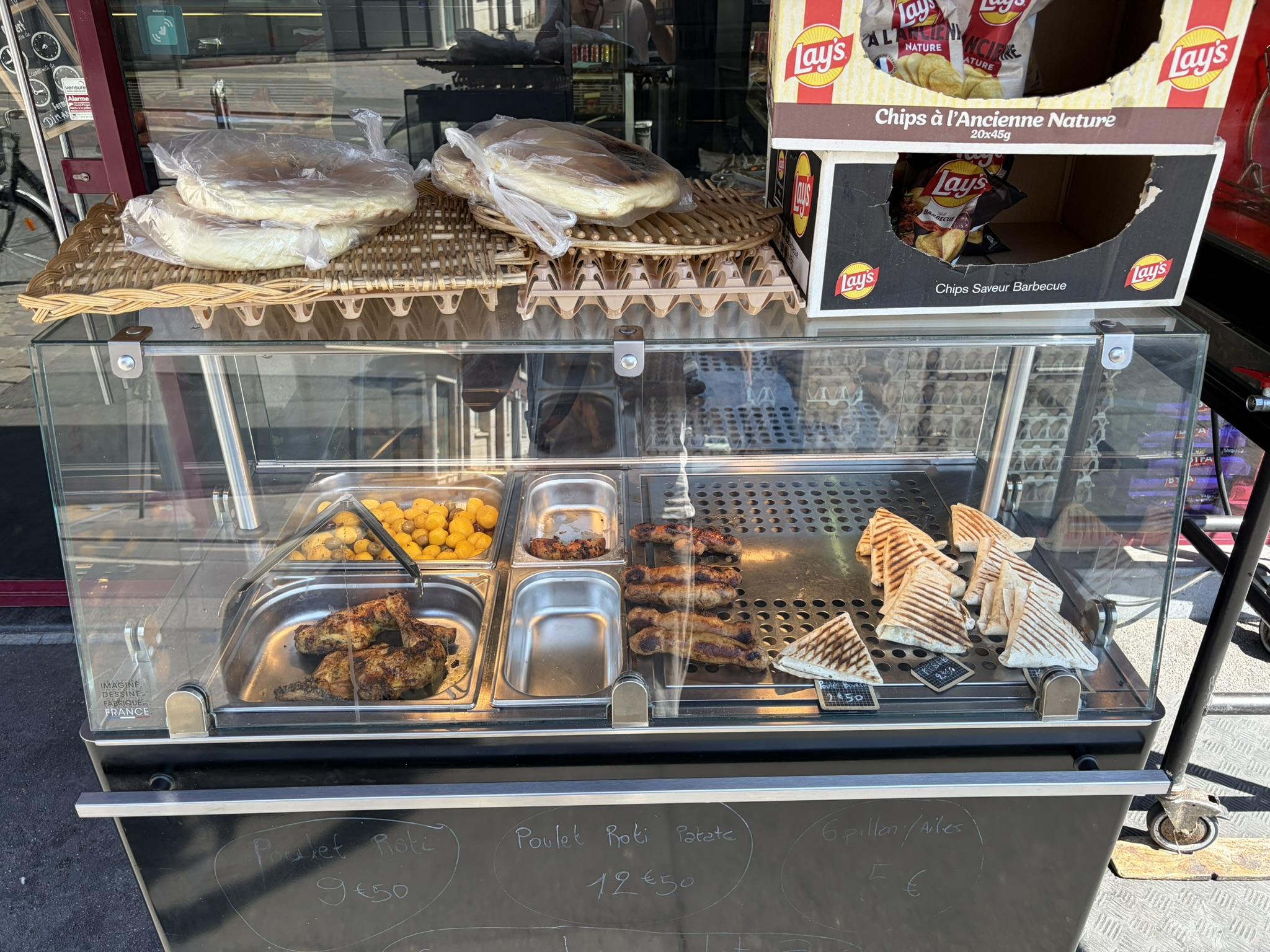 Le présentoir chaud devant la boutique : poulets rôtis, merguez, paninis et galettes